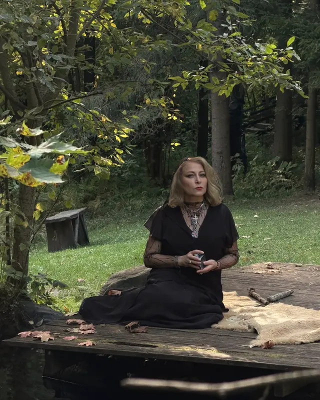 Alice sitting on a wooden jetty above dark water, a deck of cards in her hands, a sheepskin beside her